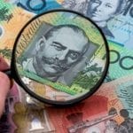 Magnifying glass focusing on an Australian banknote – Financial advice on scrutinising investments and making informed financial decisions.